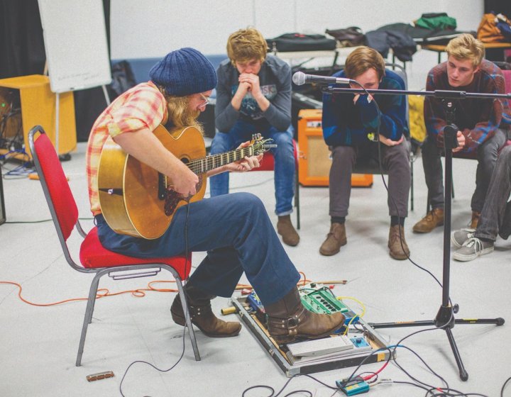 A man plays his guitar in front of three young men